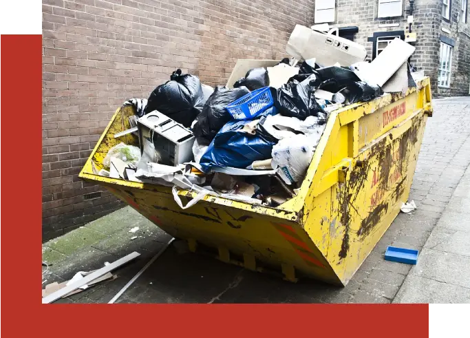 A yellow dumpster full of trash next to a brick wall.