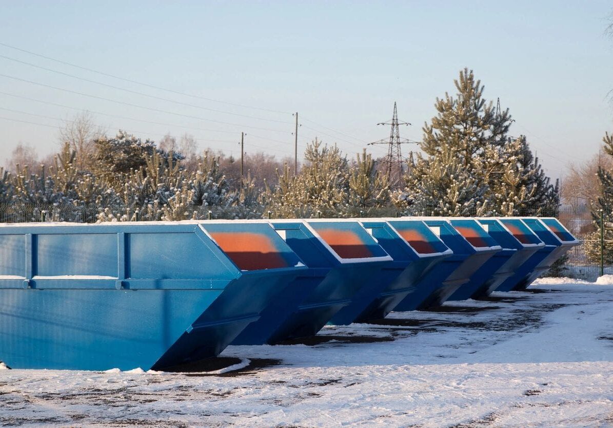 A row of blue dumpsters in the snow.